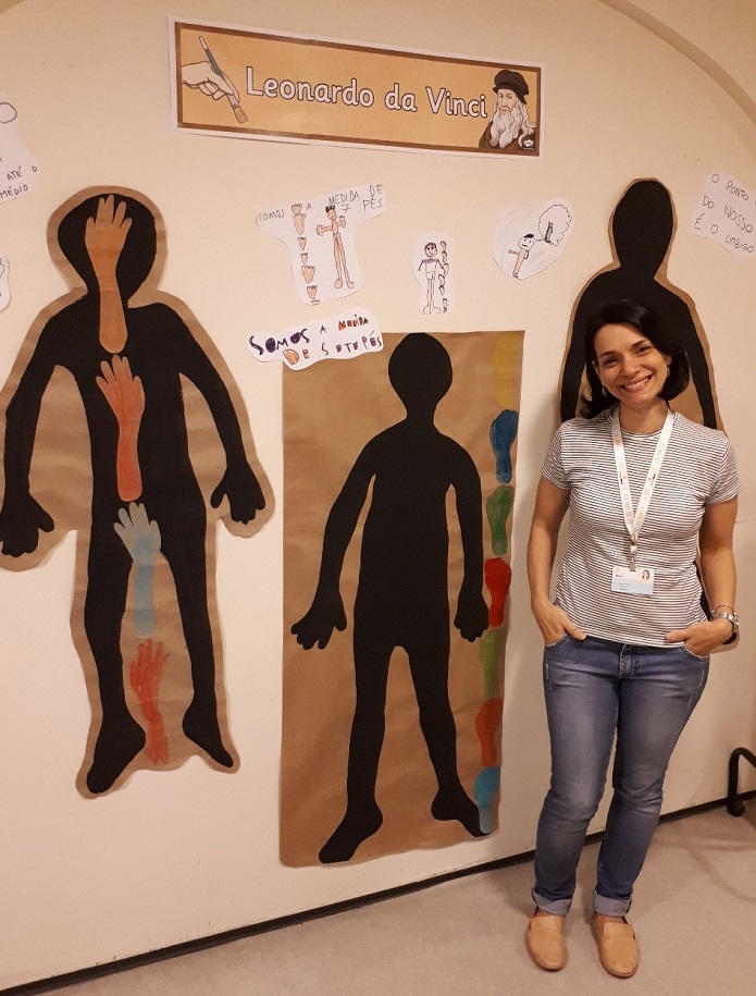 Professora diante de cartazes e desenhos criados por estudantes